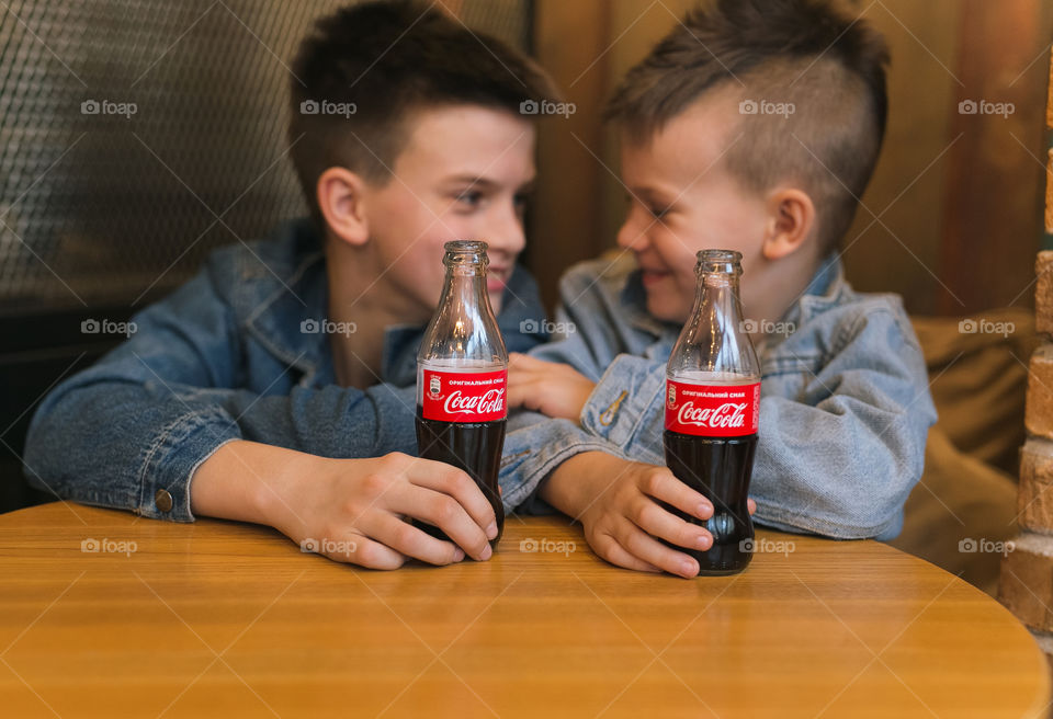 two brothers, sitting in a cafe, drinking cola and having fun. Tasty coca-cola