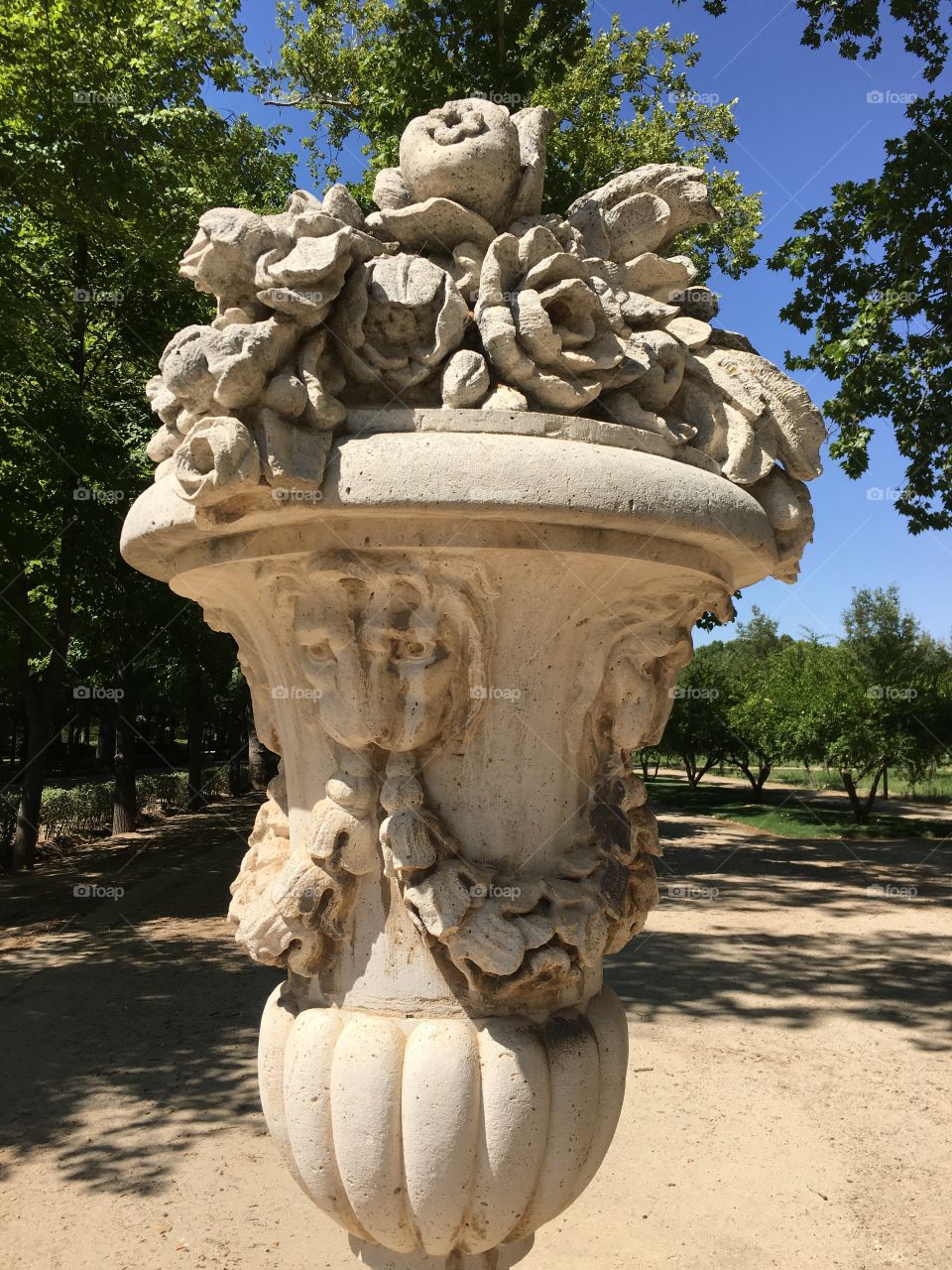 Limestone sculpture depicting a vase with gorgeous flowers on top. Decorative sculpture in the middle garden.