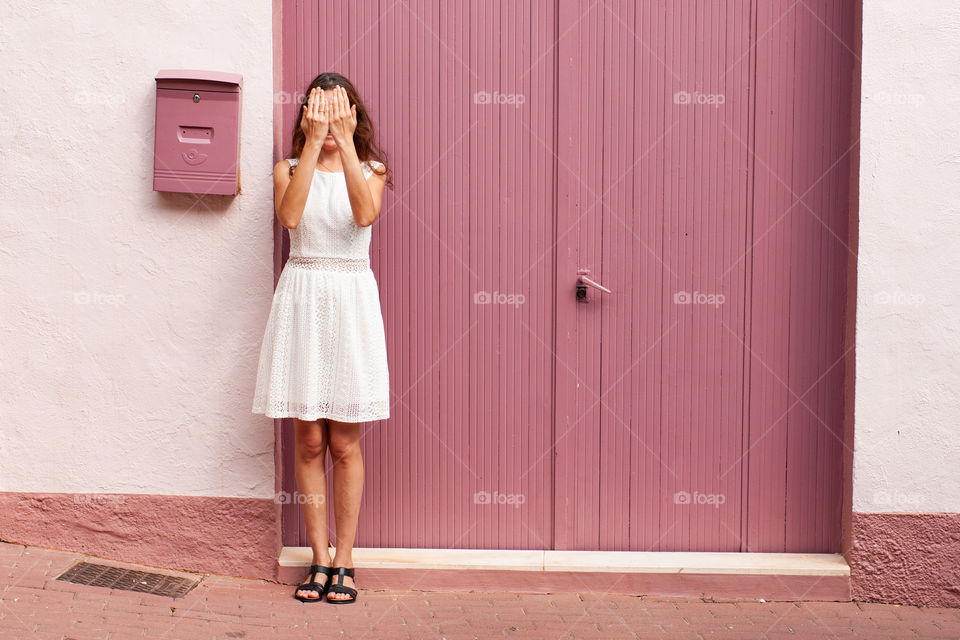 Girl in a white dress near a large pink door and a mailbox.