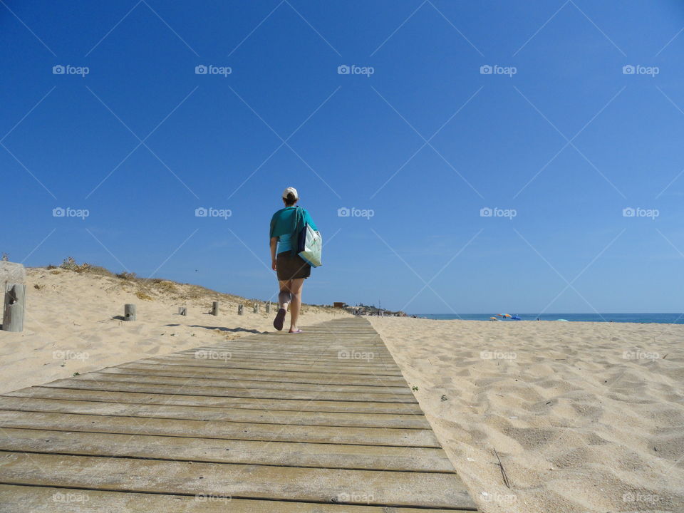 A portrait of a girl walking on a wooden plank trail on the beach on a sunny cloudless summer day.