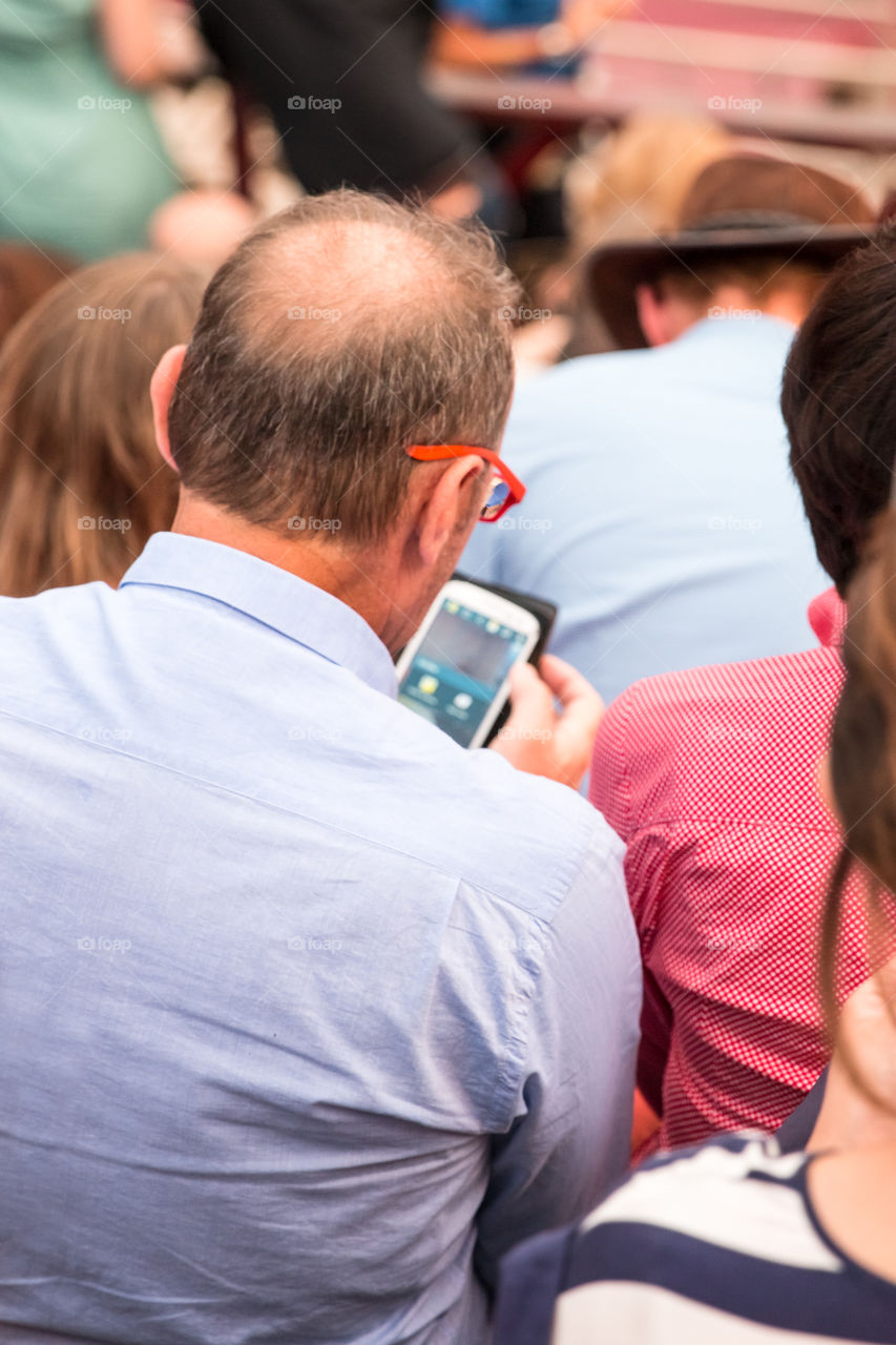 Senior Man Using His Smartphone At An Outdoor Concert
