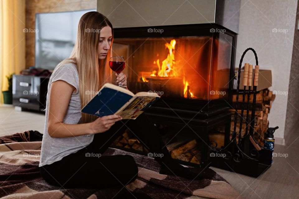 Woman drinking red wine near fireplace at home at winter 