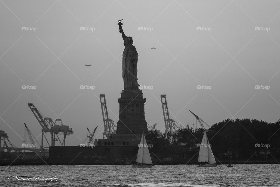 The iconic and historic Statue of Liberty is shown in black and white along with the shipyard cranes in the Newark port