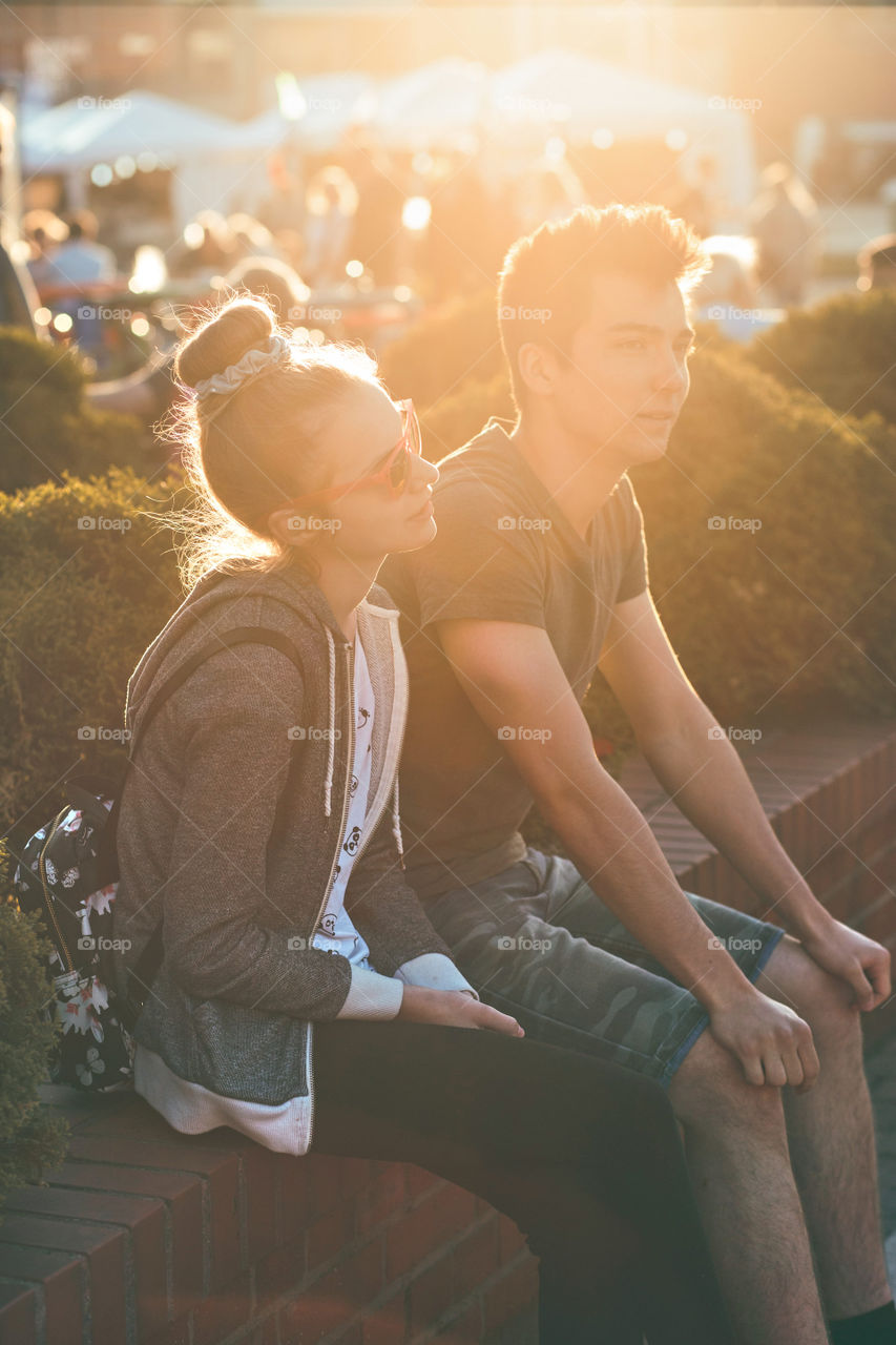 Couple of friends, teenage girl and boy,  having fun together, sitting in center of town, spending time together