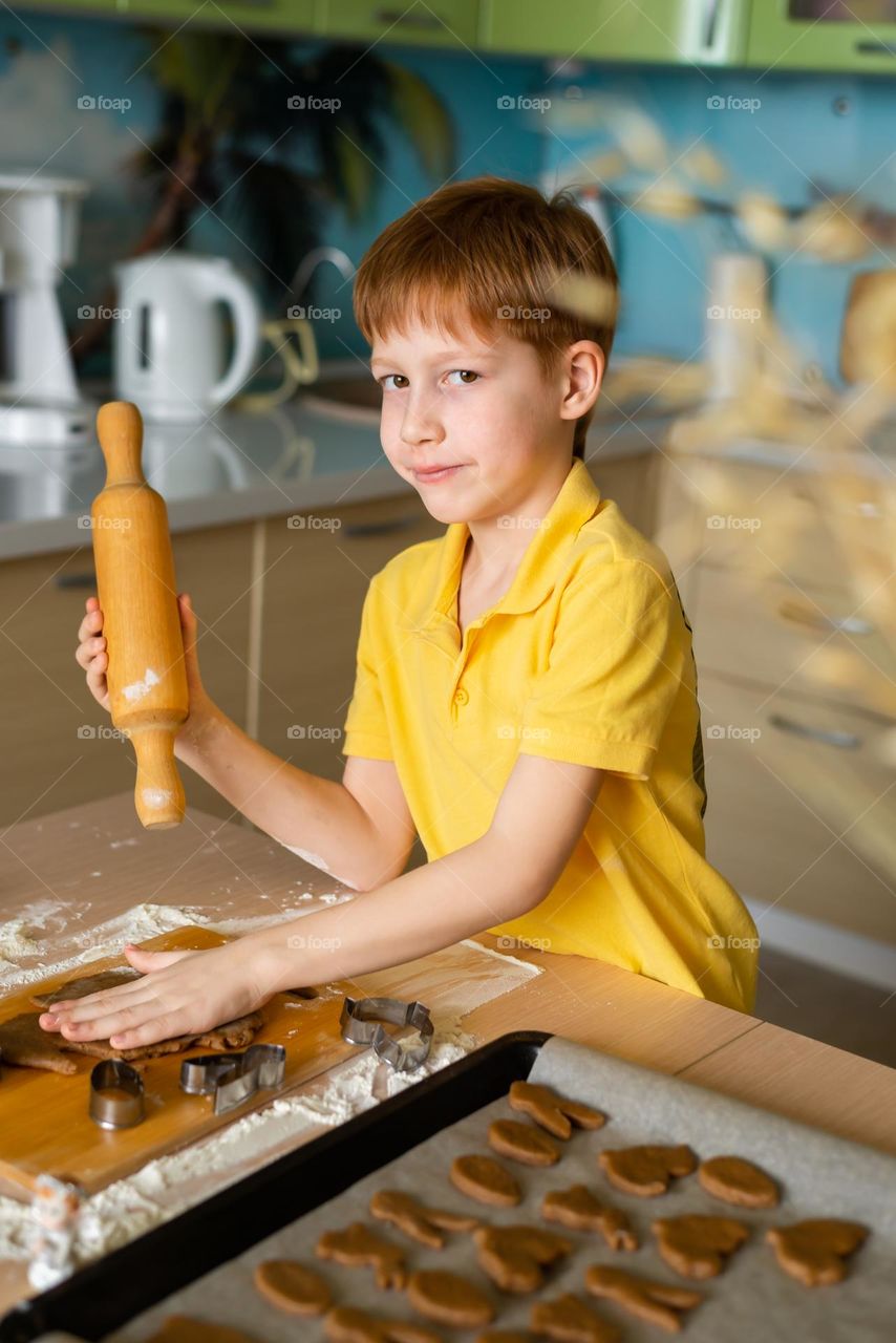 Child red-haired boy in a yellow shirt bakes Easter cookies from dough at home in the kitchen, craft product