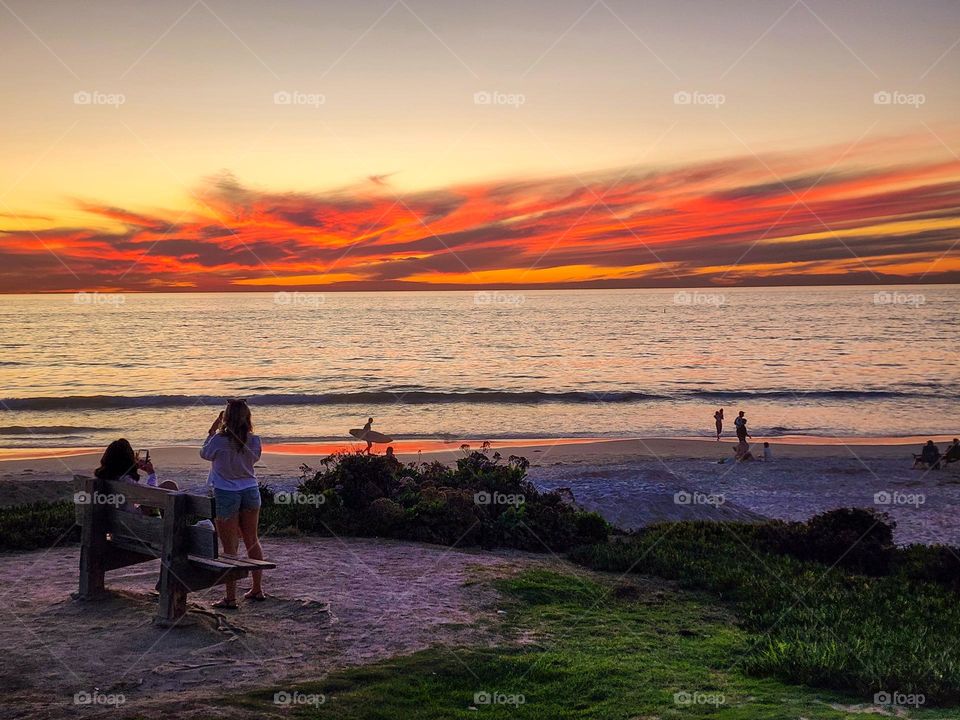 People conduct various activities on the beach on a unseasonably warm fall evening in San Diego California while witnessing a gorgeous sunset
