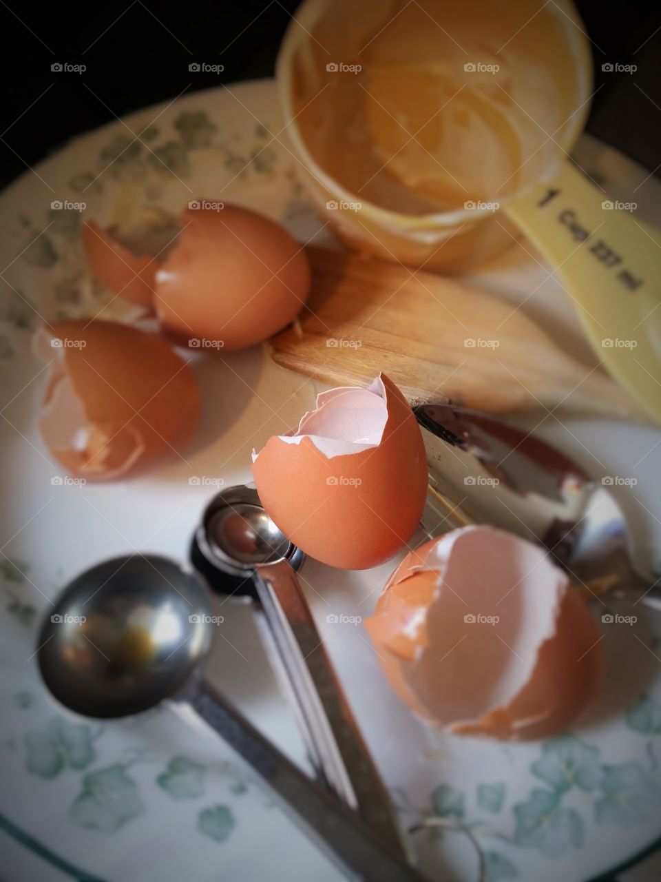 Cracked brown egg shells on a plate with measuring cup and spoons making a cake messy