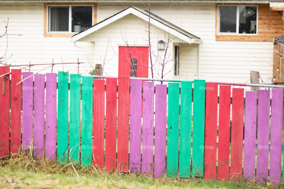 A vibrant turquoise, violet and fuschia fence surrounds a house with a fuschia door to match. This home is in a nearby village known for its colourful public art.