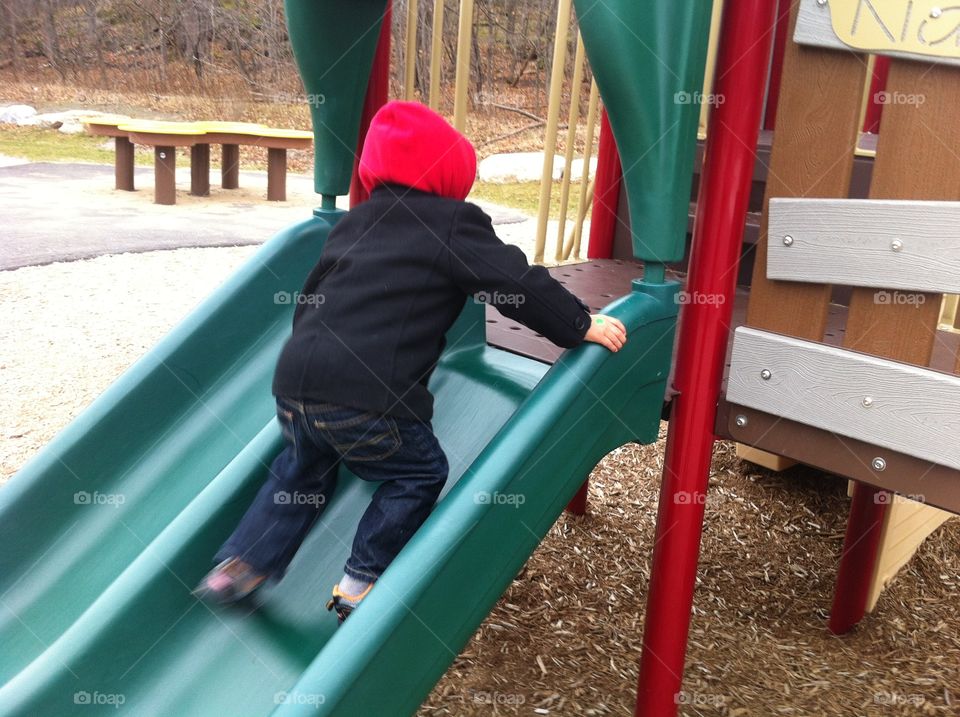 Toddler boy climbing up a slide at a children's playground.
