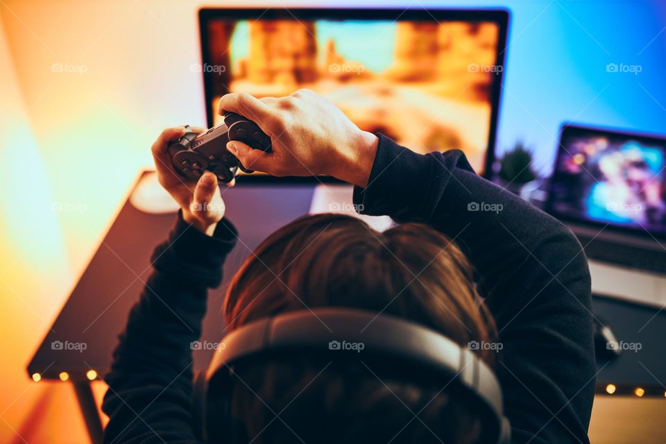 Man playing video game at home. Gamer holding gamepads sitting at front of screen. Streamer playing online in dark room lit by neon lights. Competition and having fun