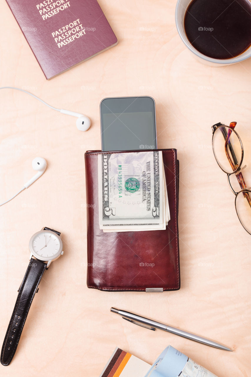 Wallet, dollar banknotes, smartphone, passport, earphones on the wooden desk. Tourist essentials. Things related to travel. Portrait orientation