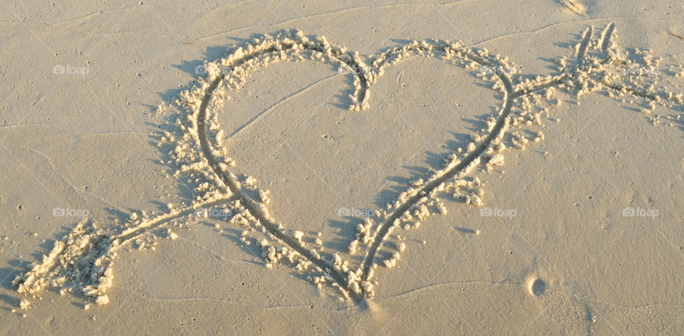 Heart with an arrow through it drawn in the sand at the beach