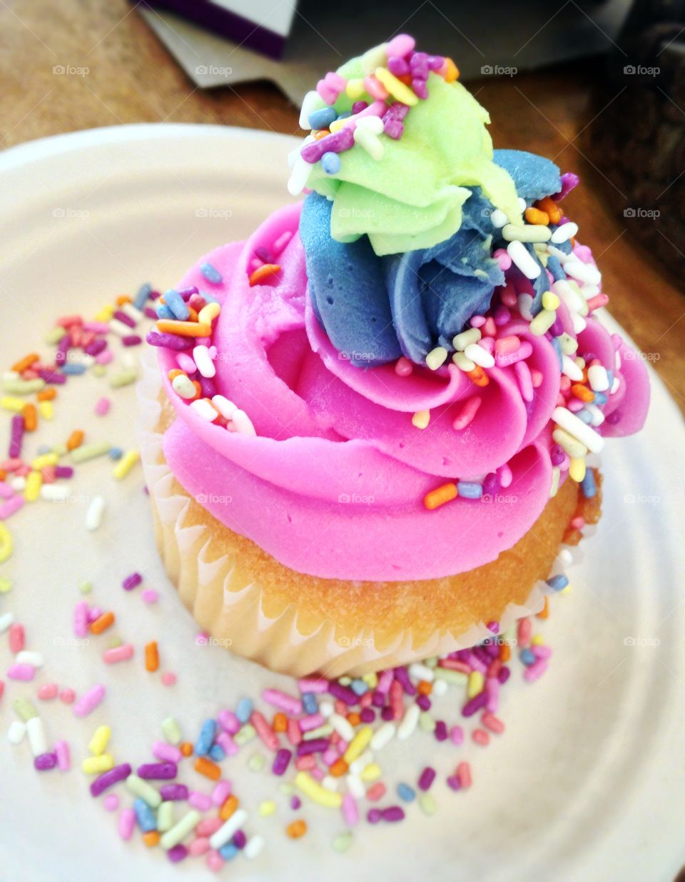 Festive cupcake . Frosted pink, blue and green cupcake with multicolored sprinkles 