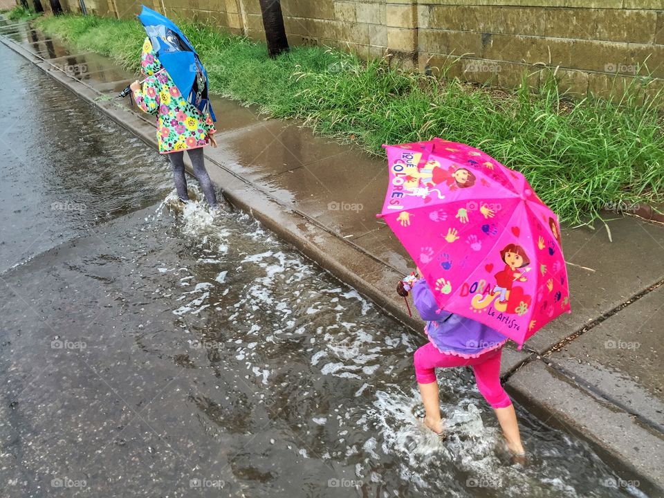 Two little girls splashing my in puddles after a summer rainstorm. 