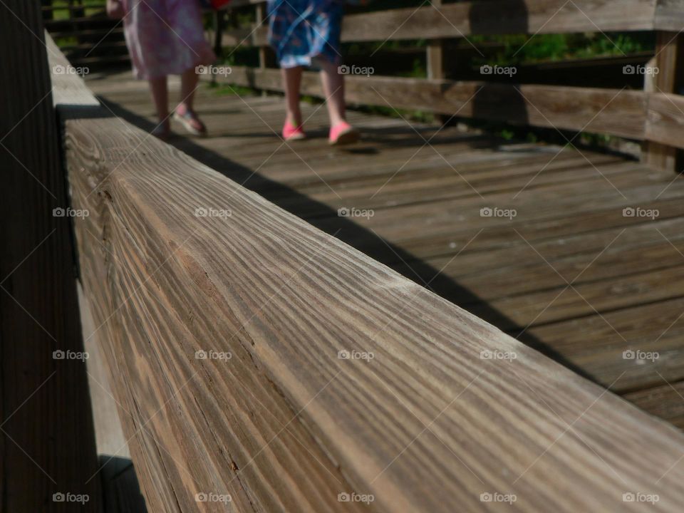 Wooden boardwalk leading to the ocean beach with two girls children walking with their body board with pink and blue modest dress swimsuits.