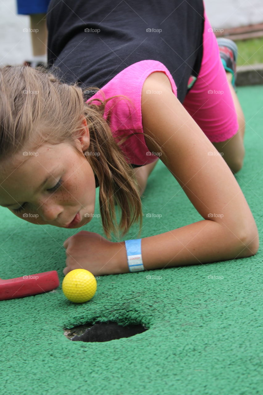 Little girl blowing golf ball in hole