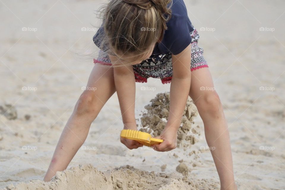 Girl digging at the beach with yellow shovel 