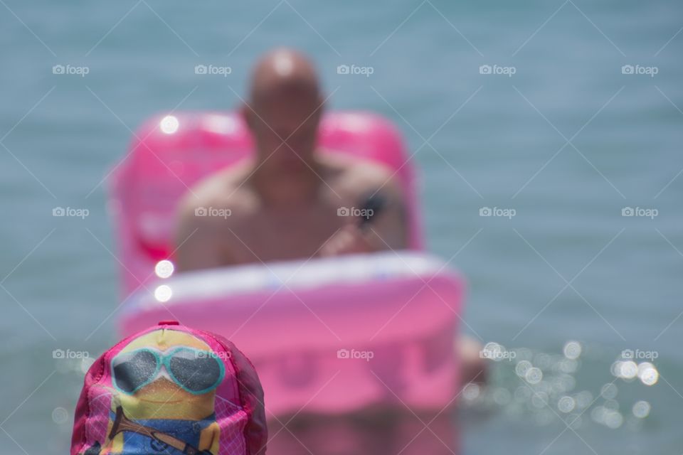 A man on an air bed in the ocean, and his little girl with her funny minion cap in spain