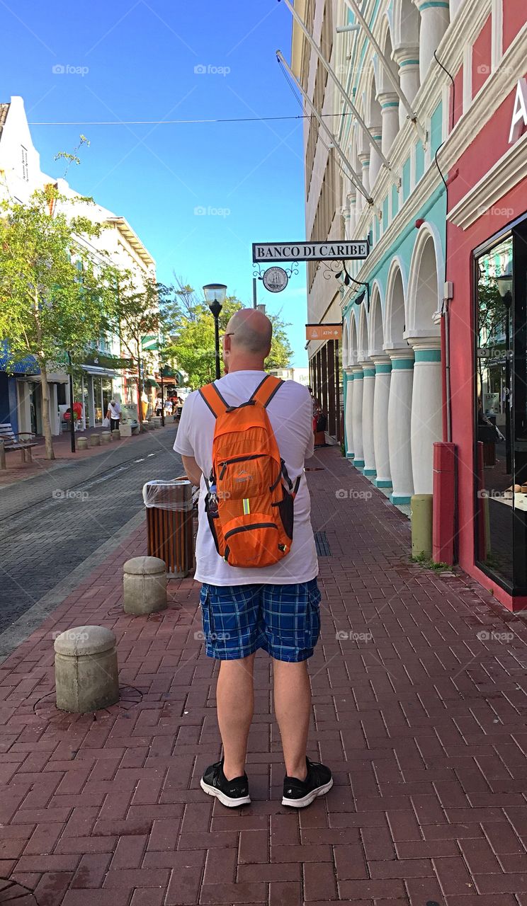 Surveying his surroundings - Middle-aged man with an orange backpack standing on the sidewalk. 