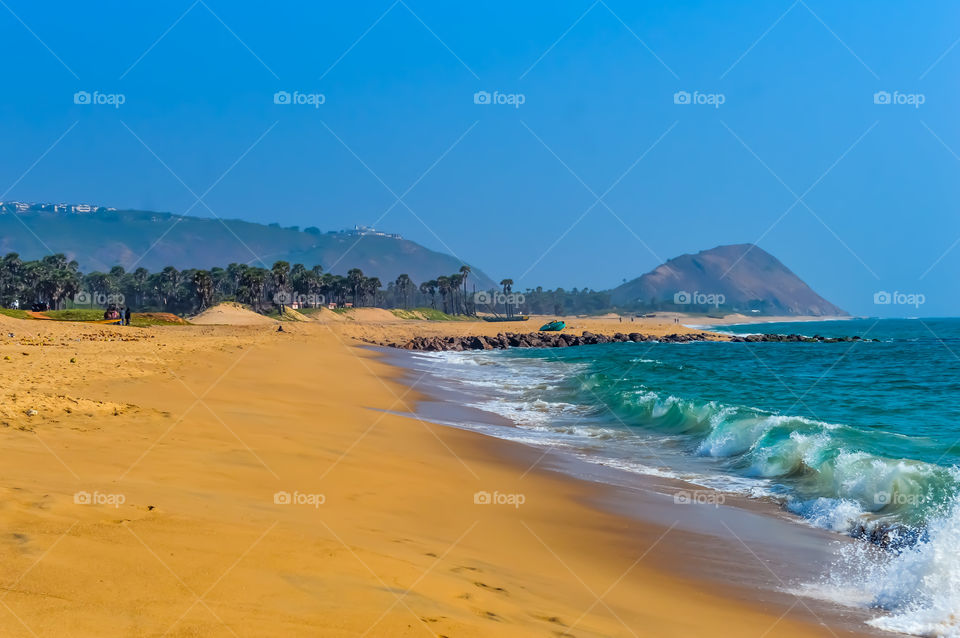 Wild Empty Tropical beach, vibrant yellow sand, bright blue sky, crystal clear waters with water crashing on the shore at daytime on a sunny day in in as landscape style may be used as a background, wallpaper, screen saver Travel vacation concept. Th