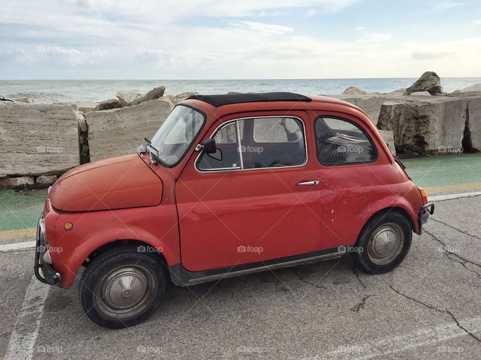 Little red car parked front of the sea