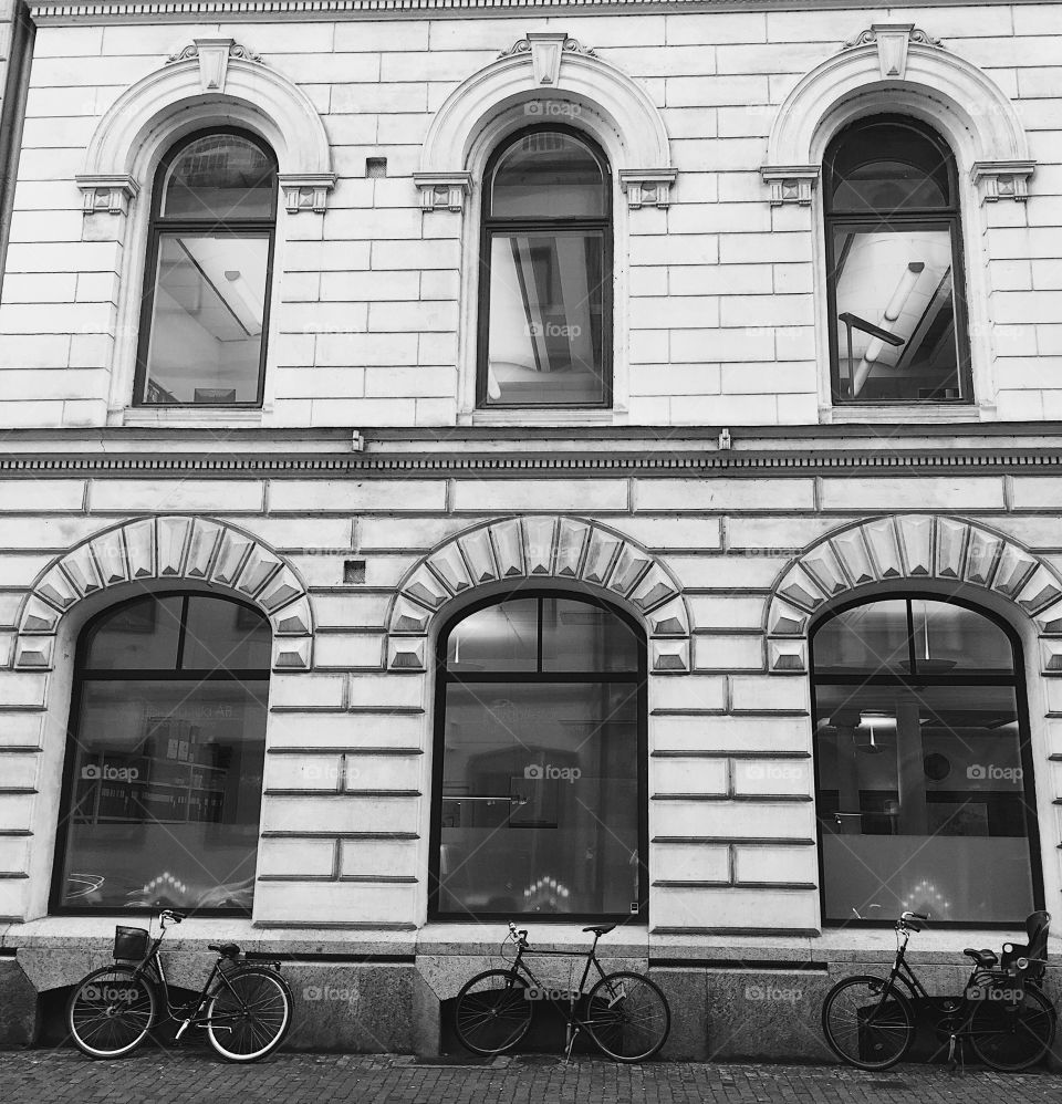 Three bikes perfectly lined up against a historic building. (B&W)