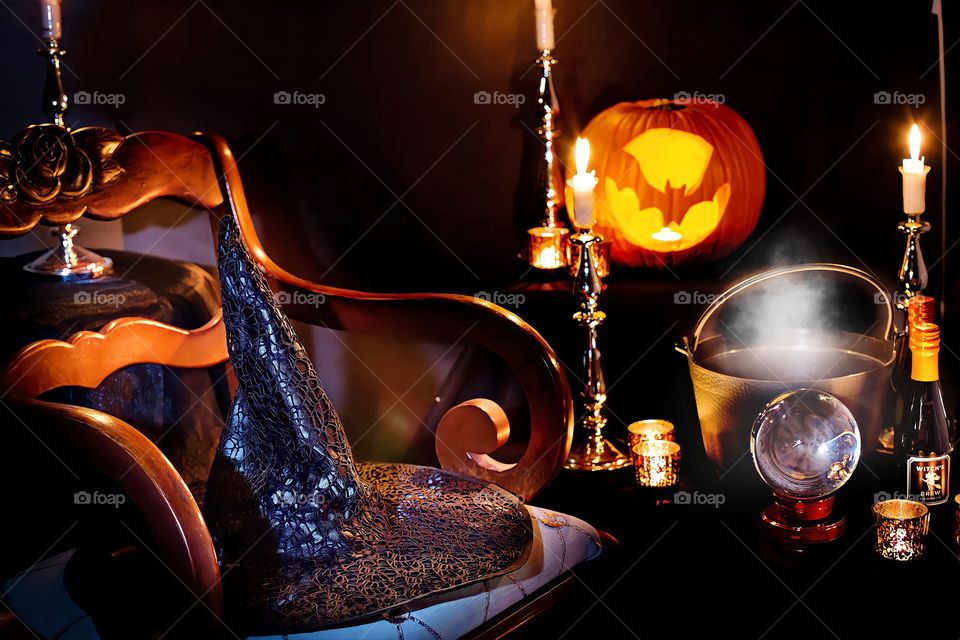 Witch hat and Jack-o-lantern.
Night View of witch hat on chair with lit candles and Jack-o-lantern in spooky room