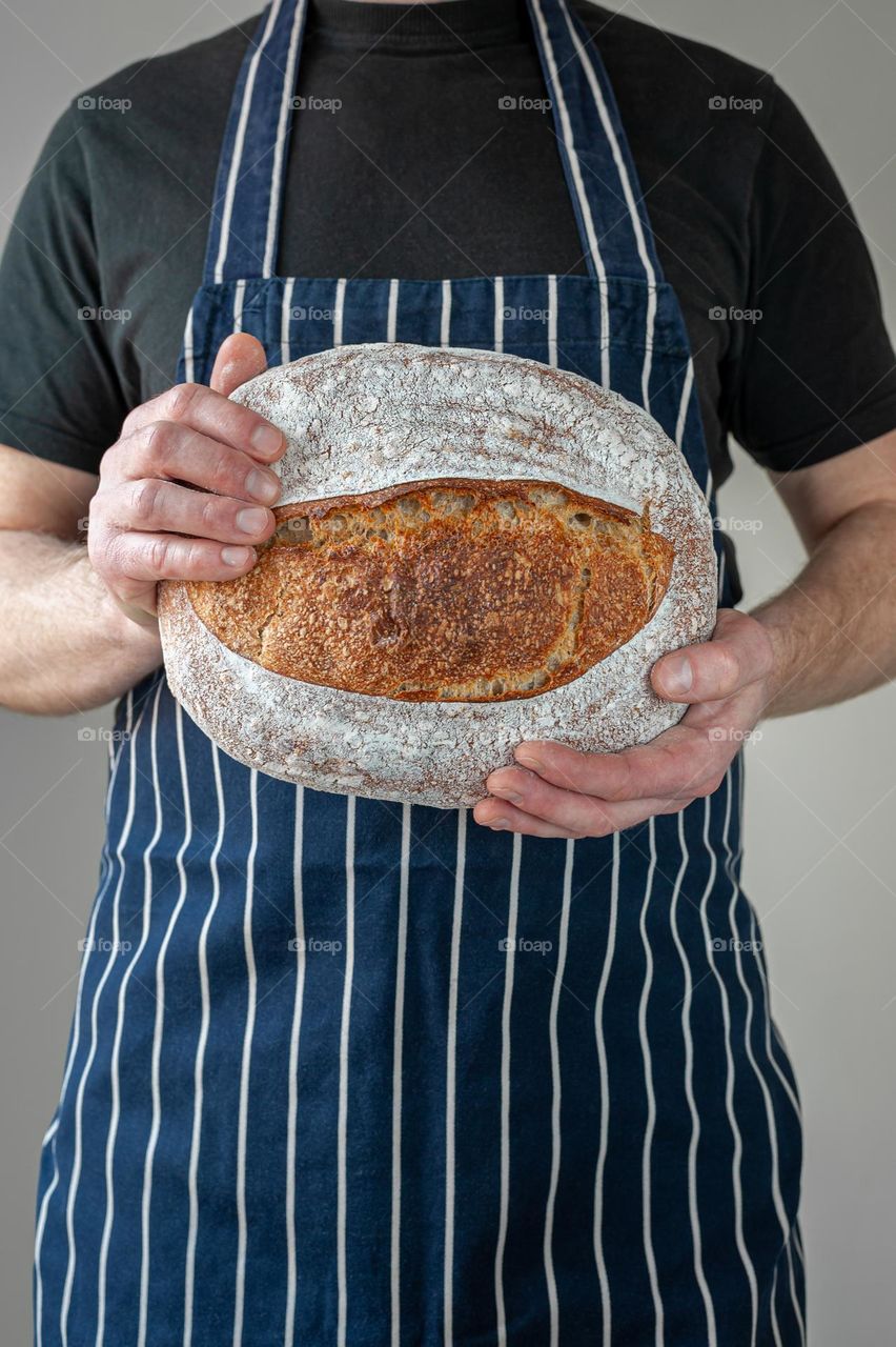 Close-up at bakers hands holding a loaf of sourdough bread in front of him.