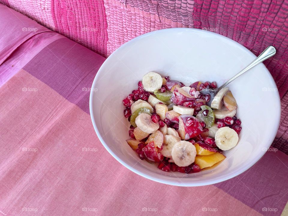 A white bowl of fruit salad on a pink couch