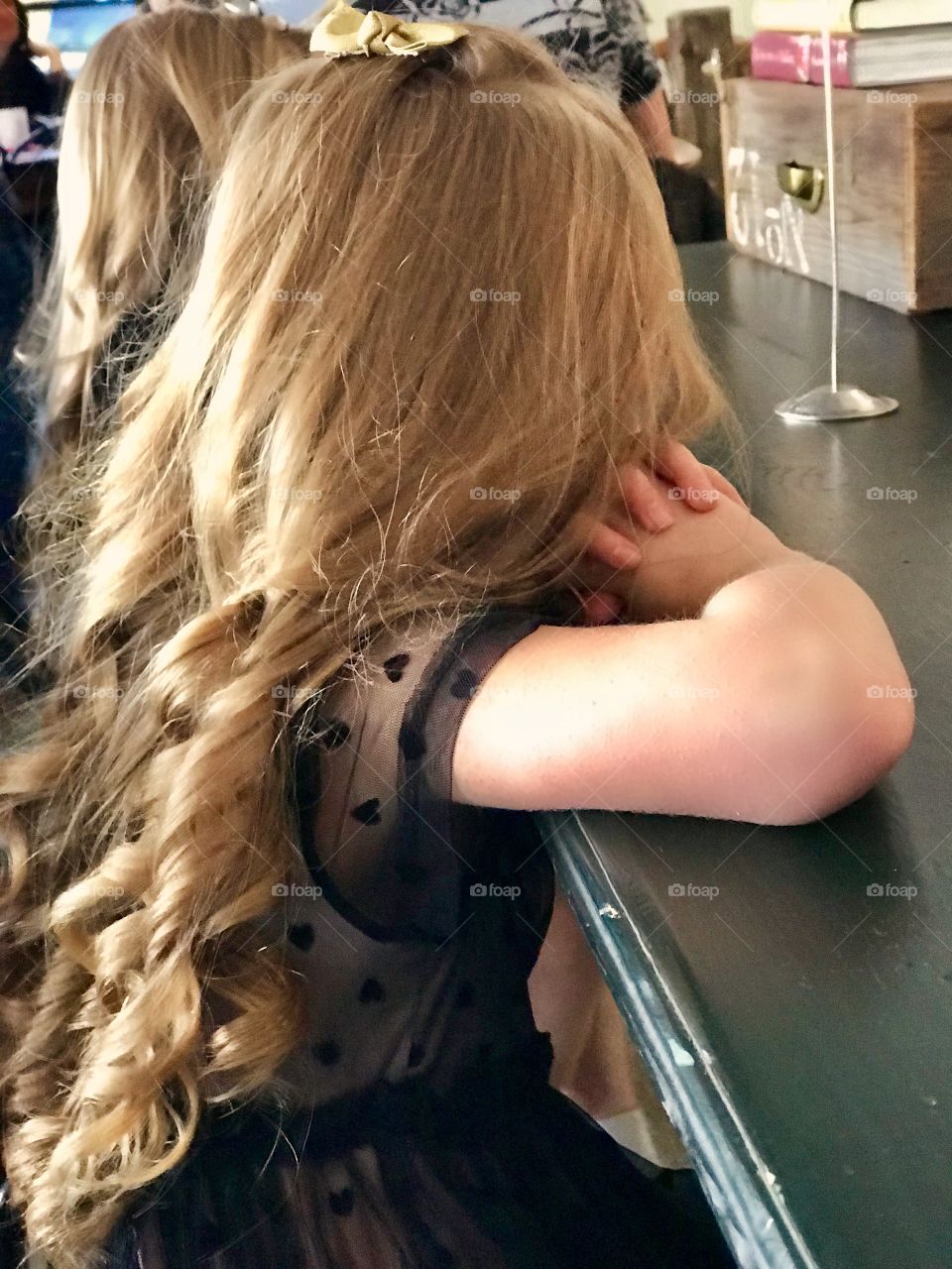 Little blond girl with ringlets waiting for food at high top table in restaurant 