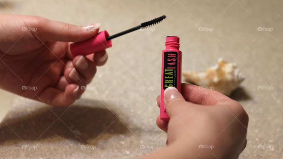 Two hands women manicured fingernails holding mascara container and wand ready for application 