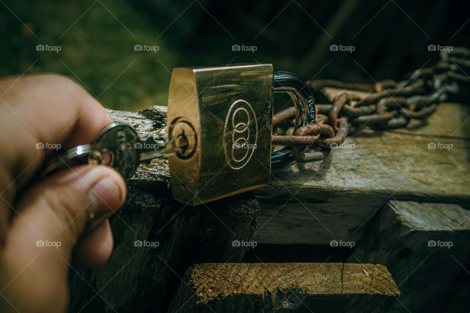 Person opening a metal lock with a key on the wood