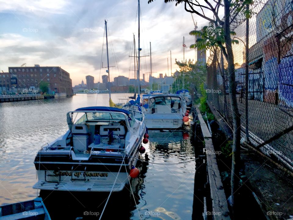 Boats in the waters of Newtown Creek in Long Island City, Queens, New York in the late afternoon to early evening as dusk approaches. This picture was taken in the Spring of 2019. Visible in the far, far distance is the Manhattan, New York skyline.