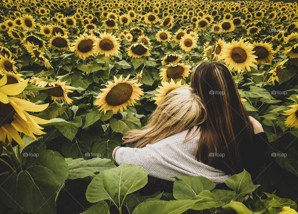Best friends taking in the last moments of summer, together in a sunflower field.