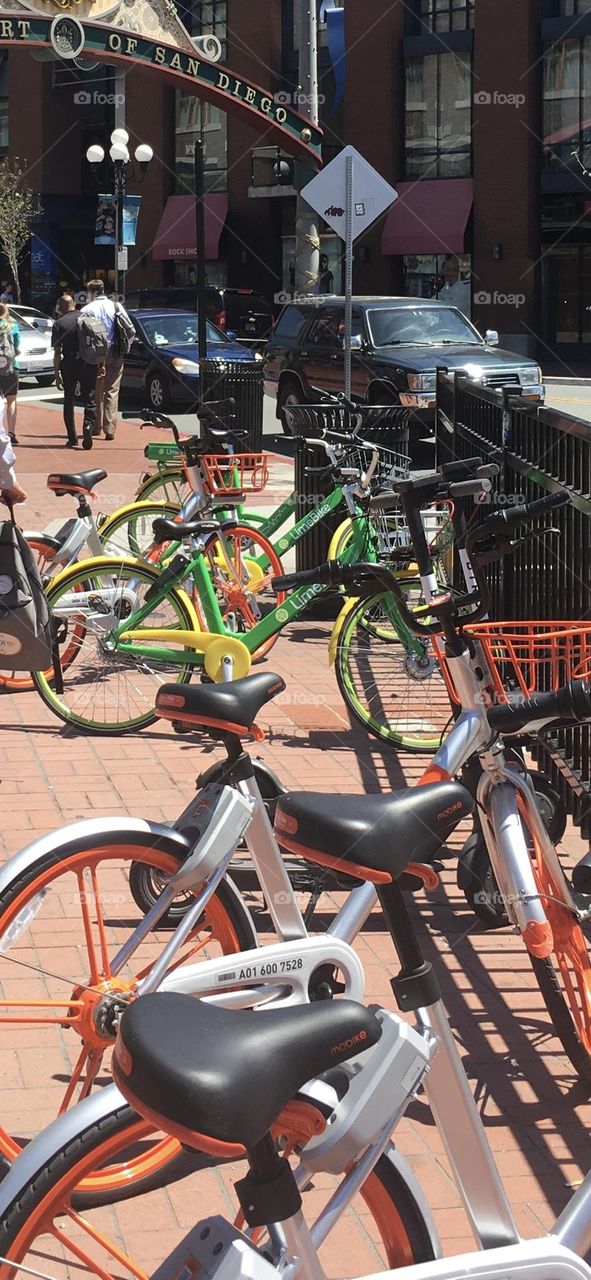 A vibrant scene of brightly colored rental bicycles lined up outside the iconic arch of the Gaslamp quarter, San Diego. The bikes painted in cheerful shades of yellow, green, and orange—invite travelers to explore the city in a fun, eco-friendly way.