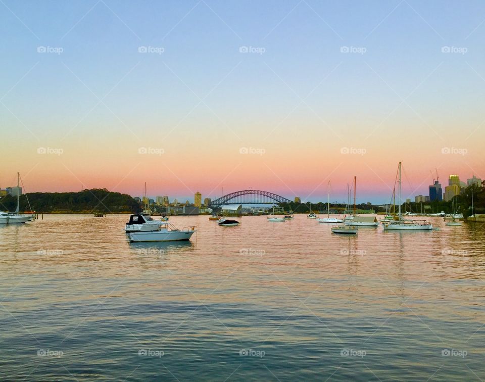 Beautiful Harbor Bridge in Sydney with an amazing pink and blue sunset sky meeting the vast ocean with luxurious boats 