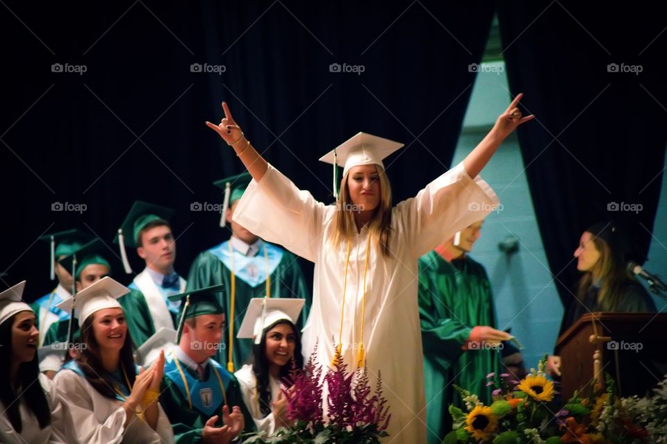 Young woman in graduation gown with arm raised
