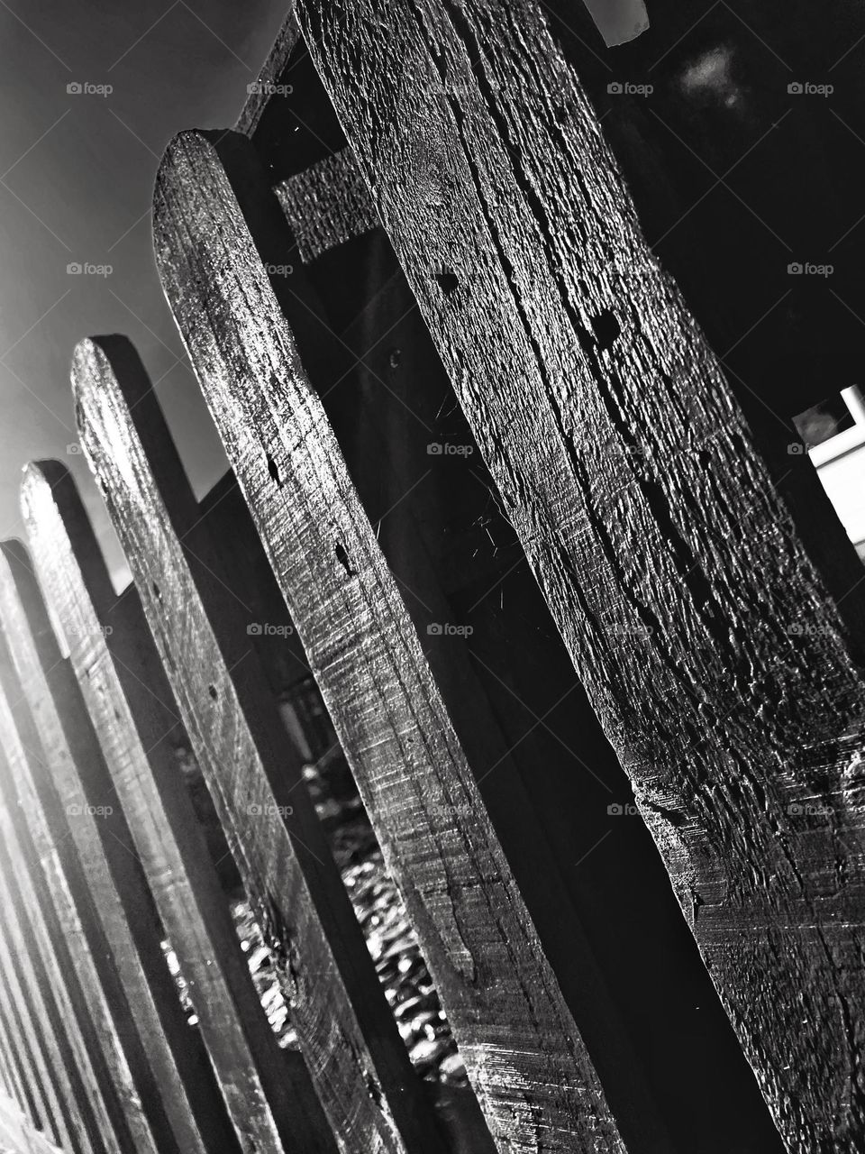 Detailed to fading close up of a wooden picket fence in black and white naturally lit by morning sunlight