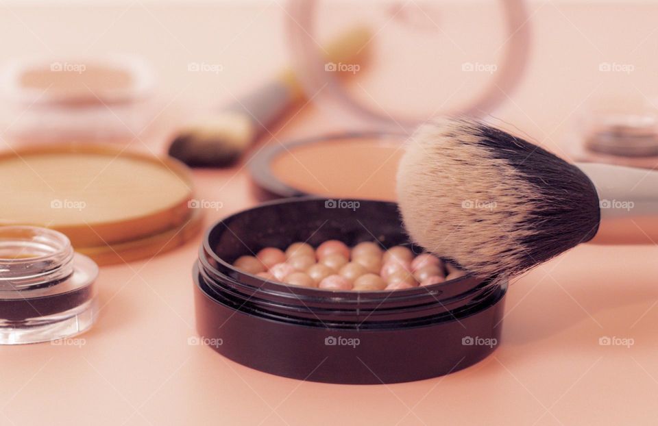 One round granular face powder with a large makeup brush with soft black eyeshadow and brow shadows lying on a pink background, close-up view from the side. Concept female cosmetics, beauty salon.