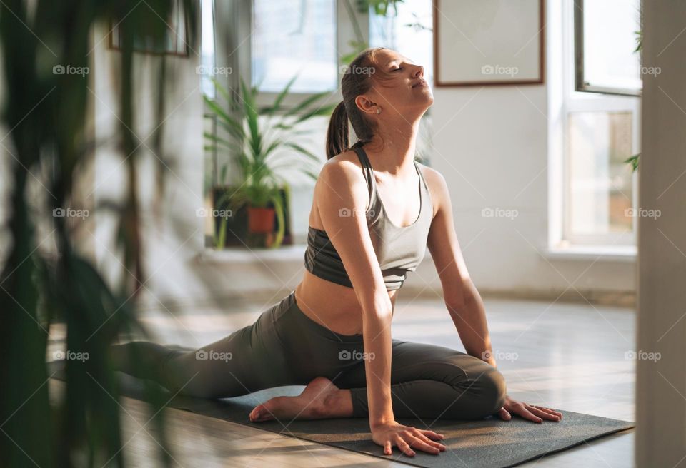 Young fit woman practice yoga doing asana in light yoga studio with green house plant