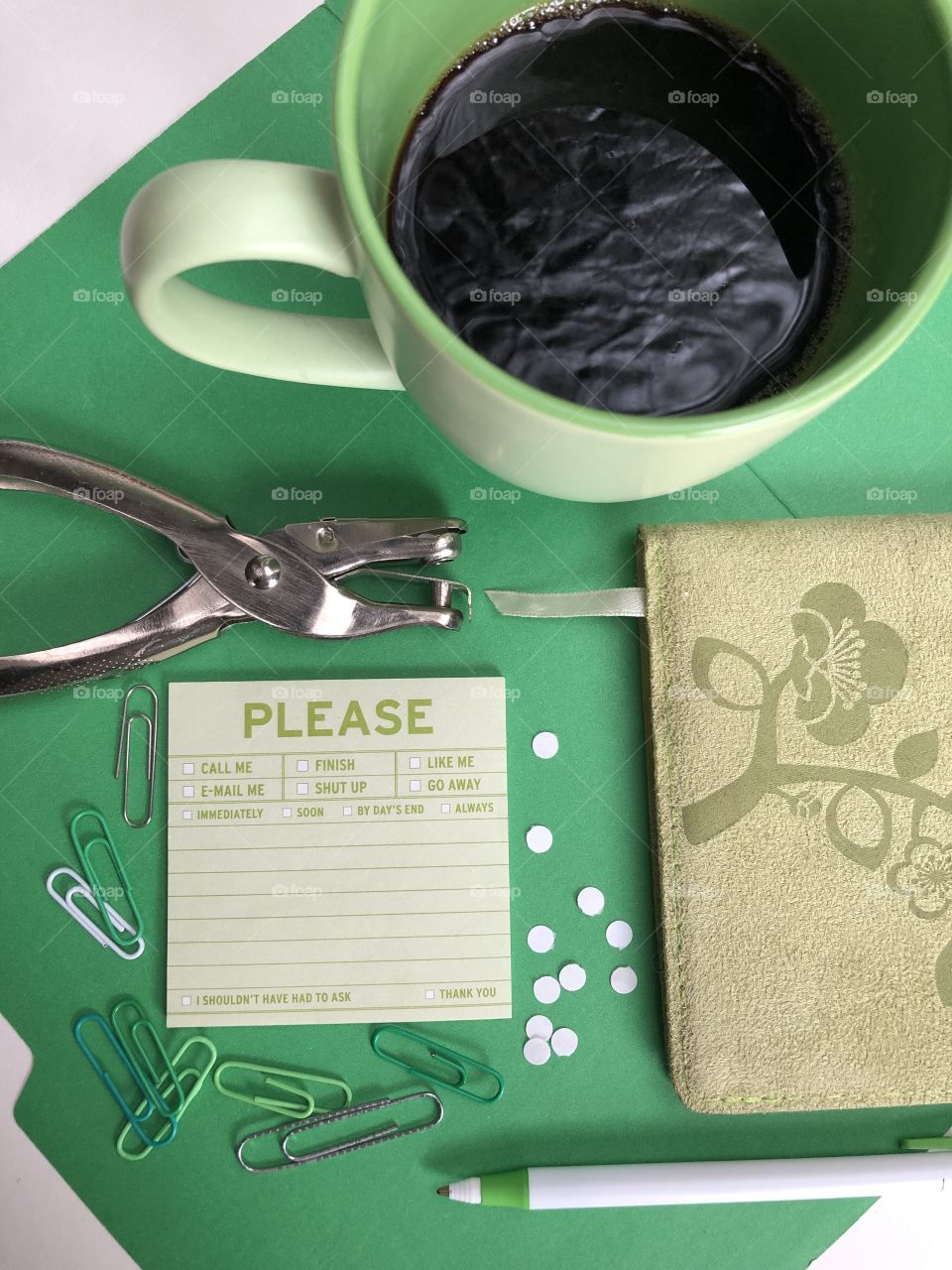 A green themed office flat lay with a mug full of coffee, a notebook and a humorous post it note