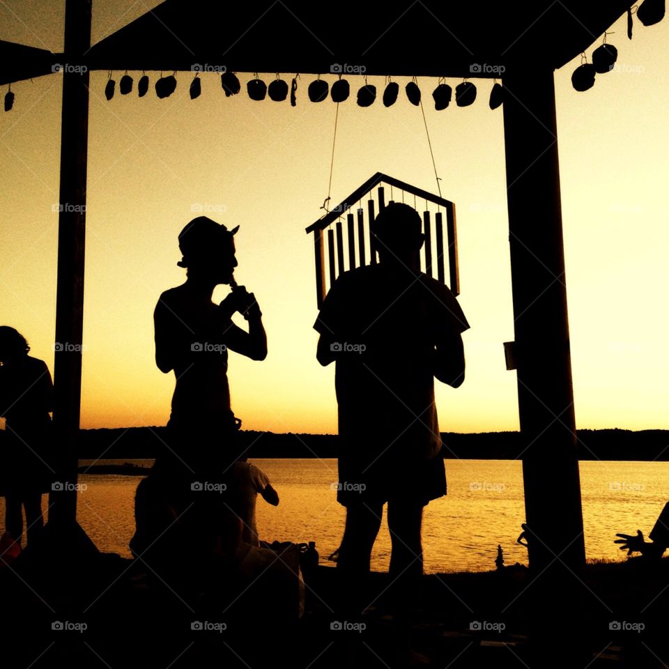 Silhouette of two musicians playing in front of a lake