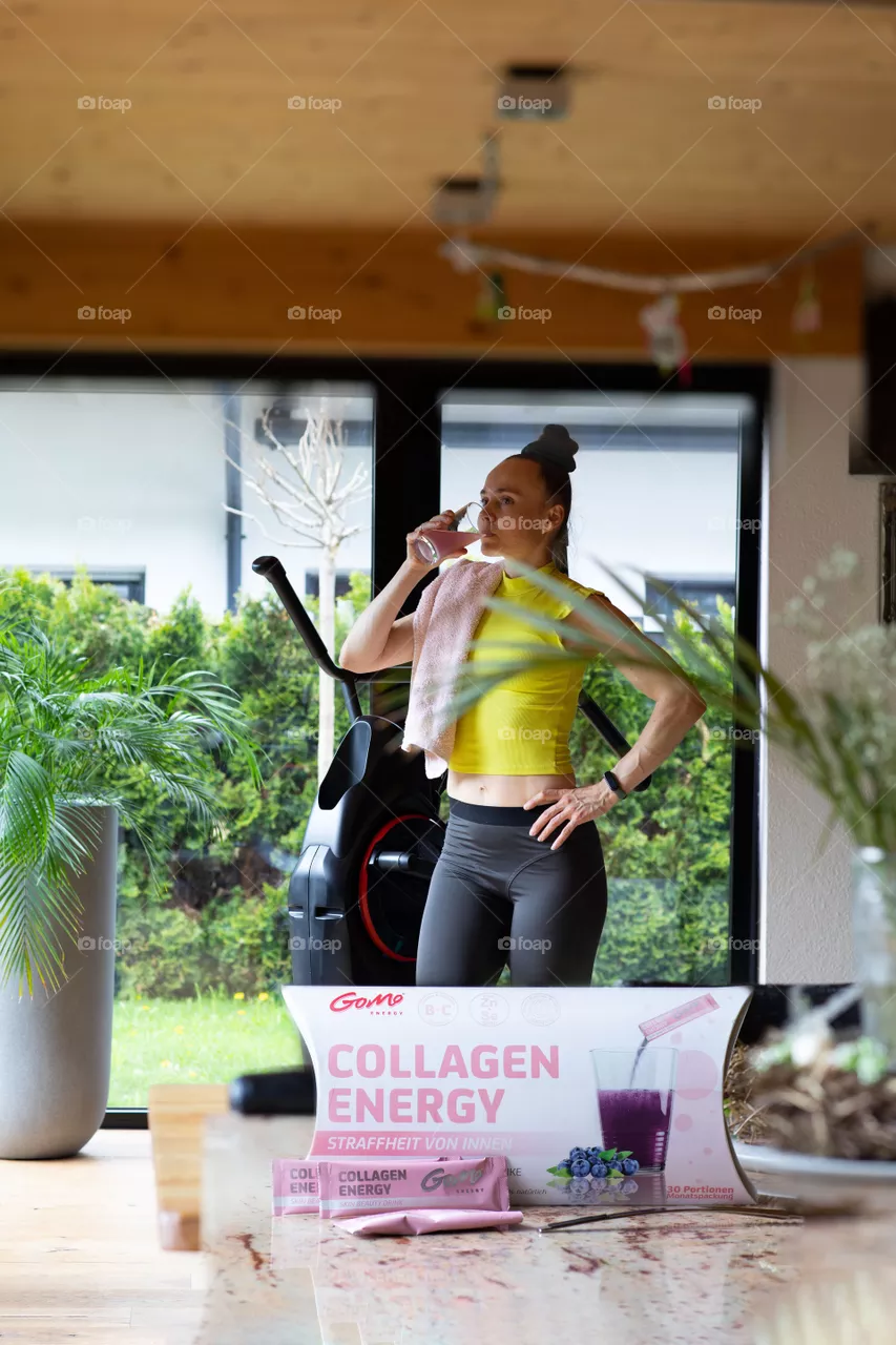 Female between 30 and 40 years old is taking GOMO collagen energy before her morning cardio. Secondary packaging of GOMO collagen energy on the table.