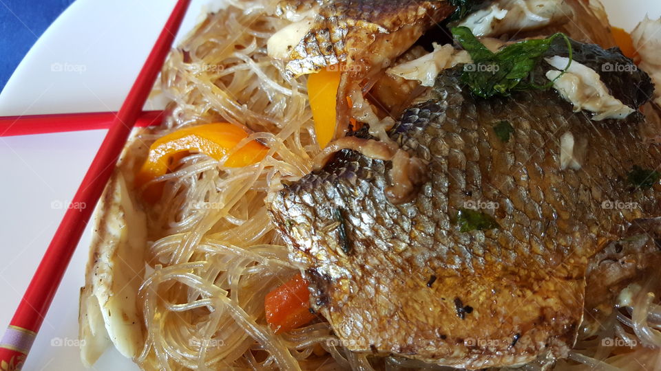 Grilled whole sea bass. with noodles, sizzled with peppers, carrots and caramelised onions. Served to eat with chopsticks and teriyaki sauce.