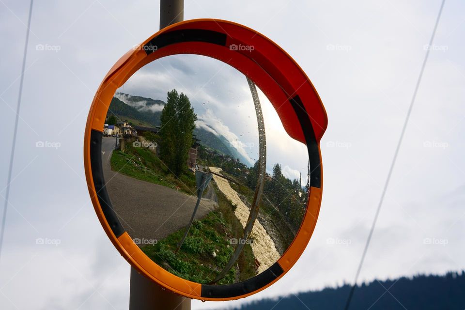 Mestia, Georgia - October 5, 2022: A road, river Mestiatchala, mountains and Mestia village seen as a reflection from a traffic mirror. 