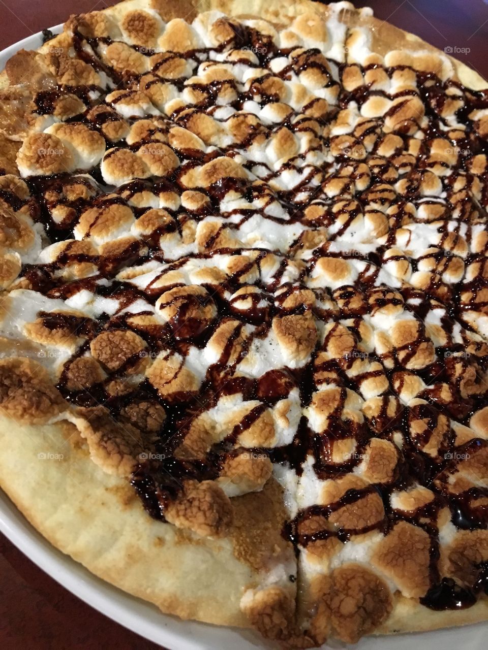 Pizza covered with peanut butter and topped with chocolate drizzle, graham cracker crumbles and marshmallows 