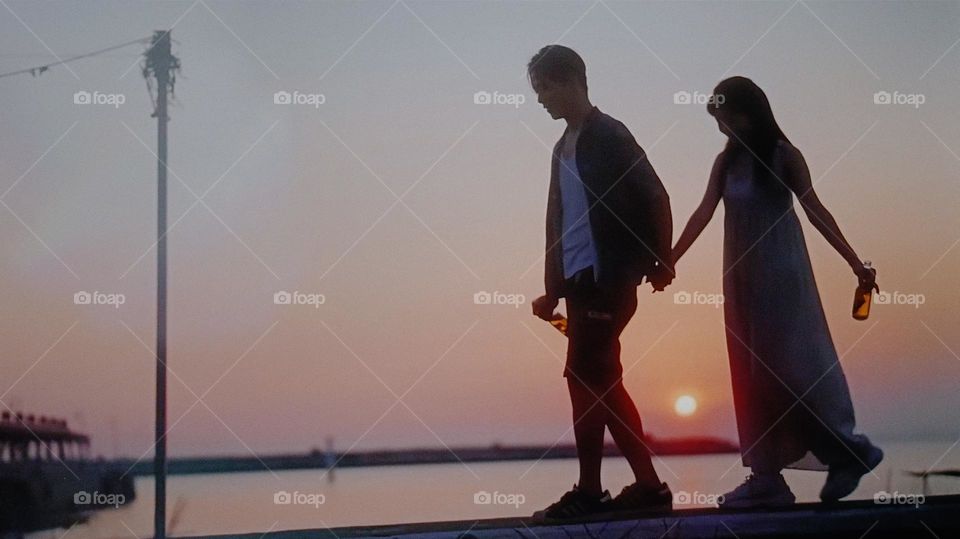 Under the sunset, a couple hold hands and walking at the seaside.