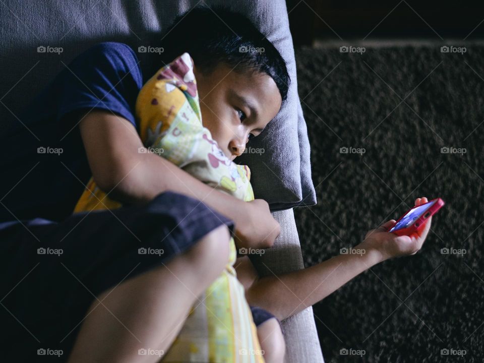 A boy hugging his favorite pillow while enjoying his phone