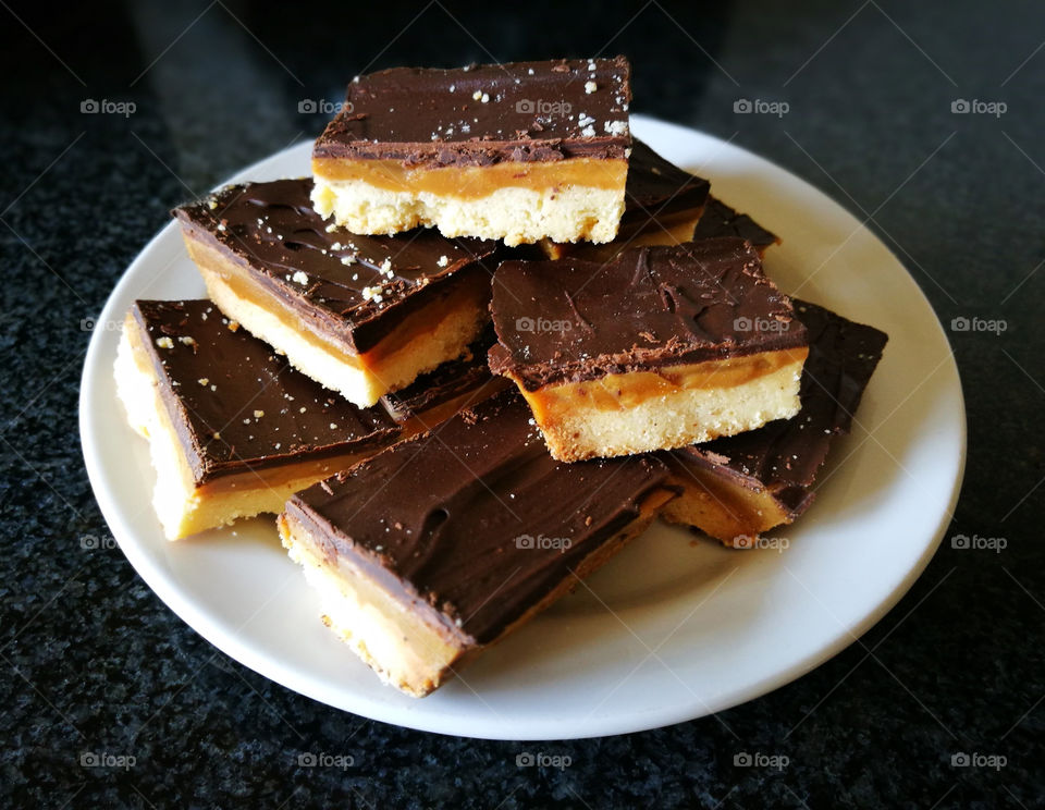 Millionaire's shortbread with chocolate and caramel slices in a white plate on black background.