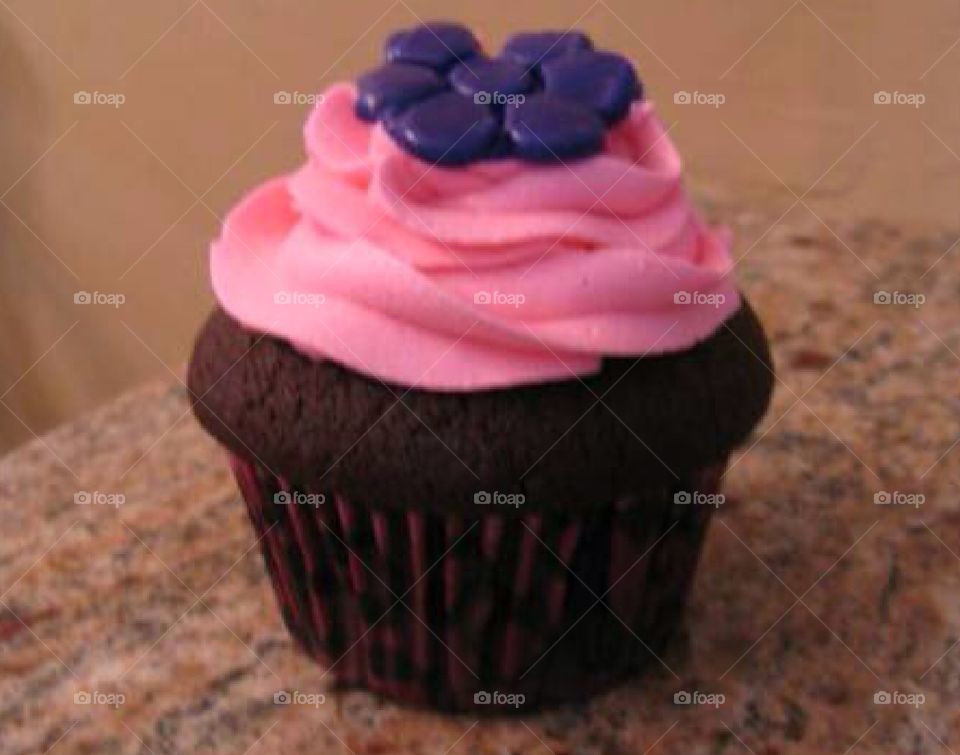 A chocolate cupcake with pink icing swirl with a purple fondant flower on top.